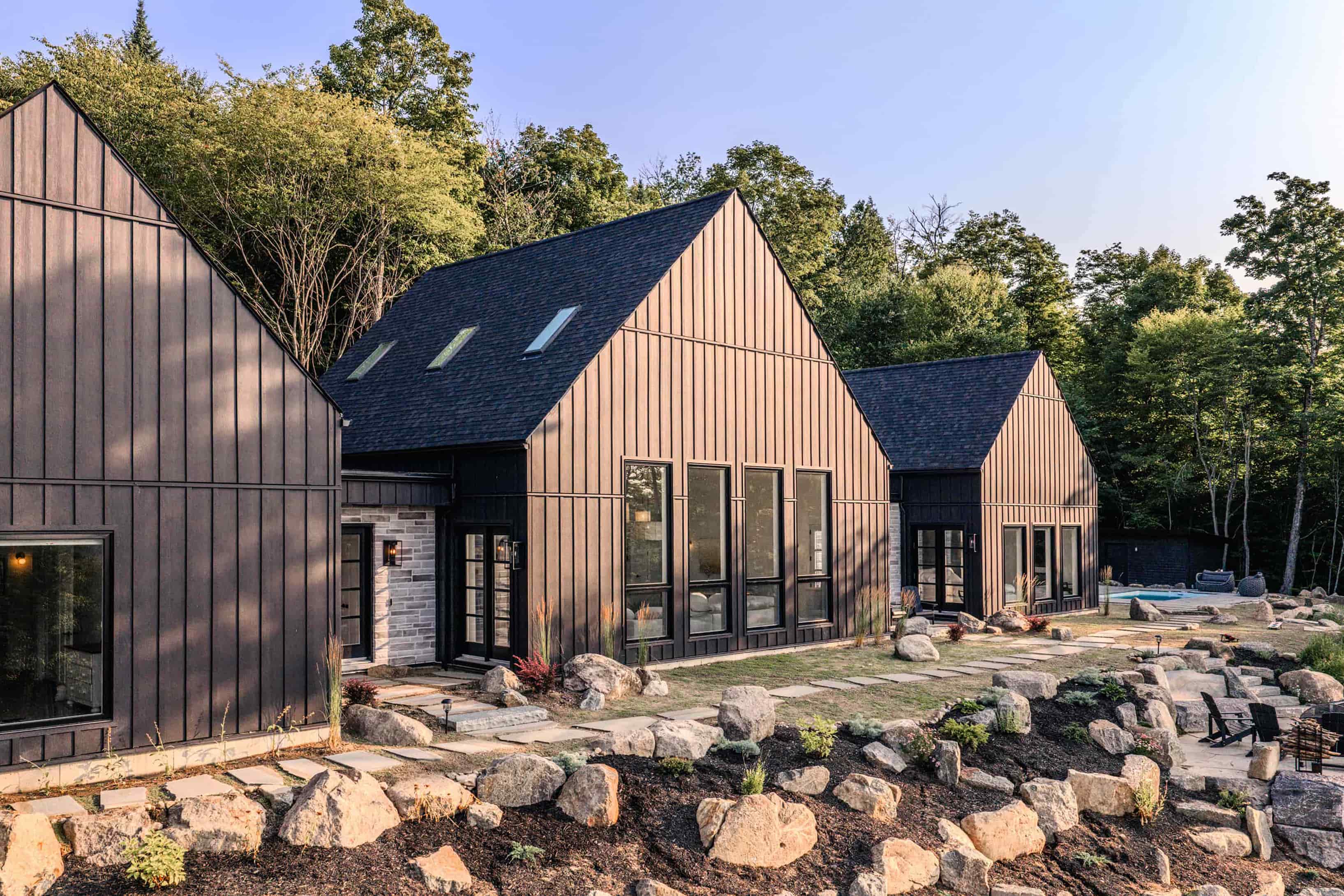 Modern black farmhouse featuring a contemporary design, situated in a picturesque forest setting, showcasing architectural design from Prim Haus house plans.