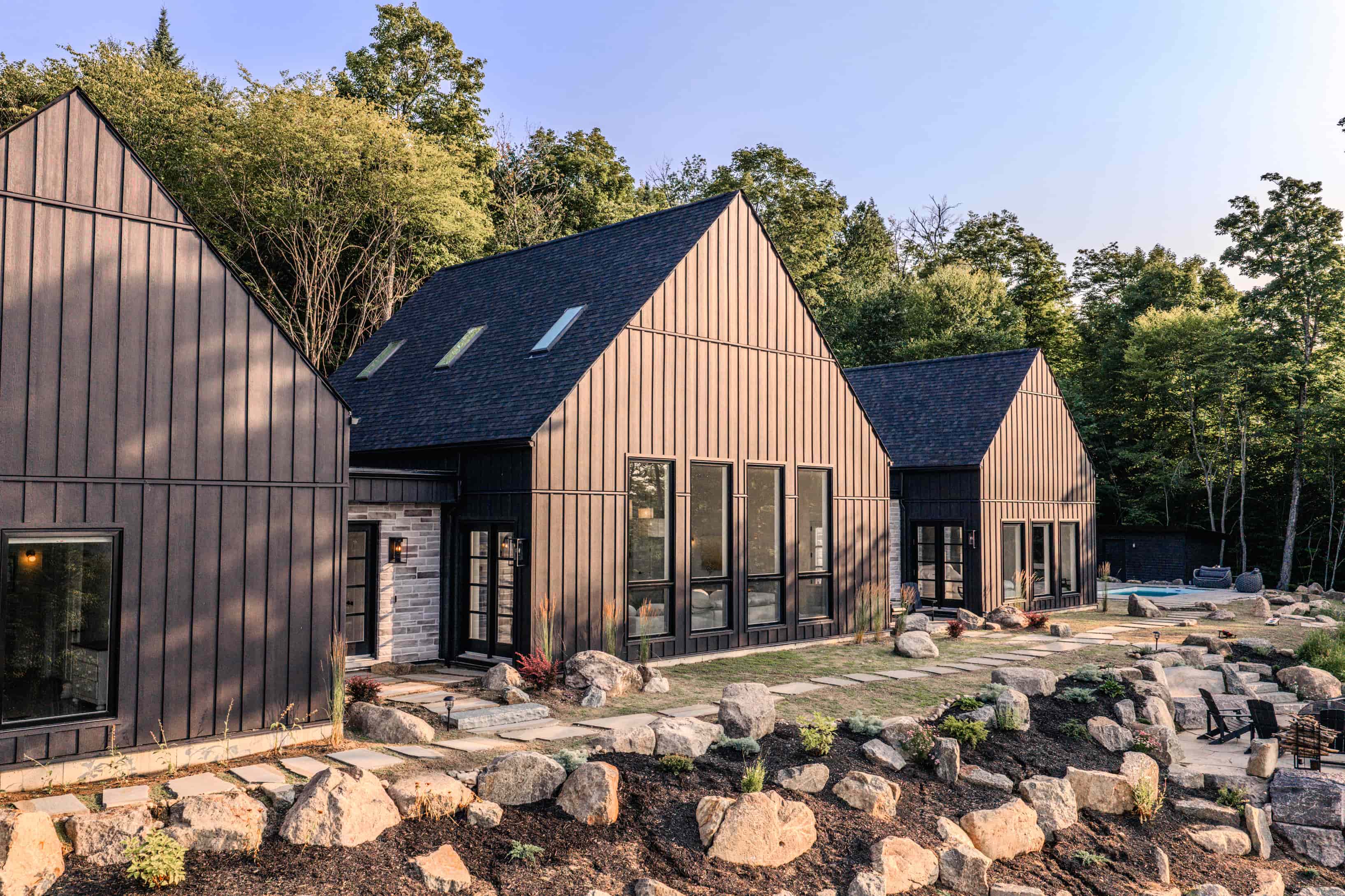 Modern black farmhouse featuring a contemporary design, situated in a picturesque forest setting, showcasing architectural design from Prim Haus house plans.